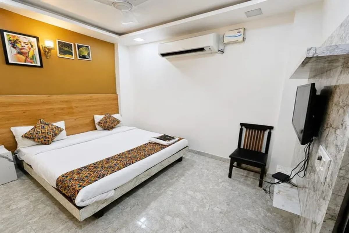 Una habitación de hotel con una cama, una silla, un televisor montado en la pared y un equipo de aire acondicionado.