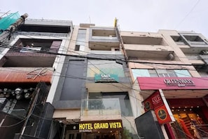 Un edificio de varios pisos con diversos establecimientos comerciales, incluyendo un hotel llamado 'HOTEL GRAND VISTA' y una tienda llamada 'GREENWAYS'.