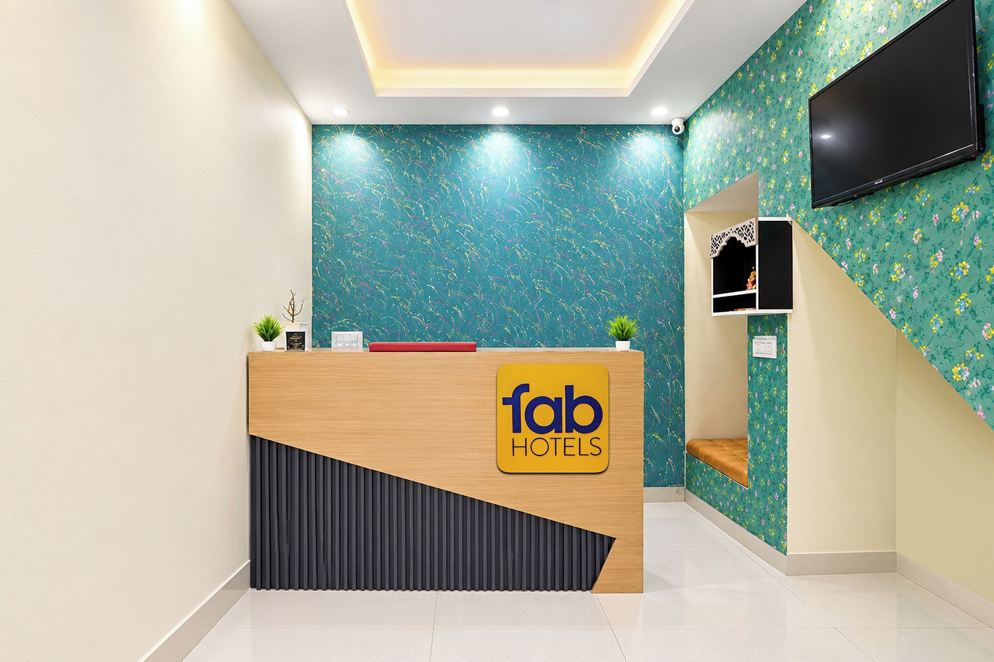 Uma receção de hotel com design moderno, uma televisão de ecrã plano na parede e uma pequena área de estar com um banco.