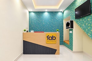 A hotel reception desk with a modern design, a flat-screen TV mounted on the wall, and a small seating area with a bench.
