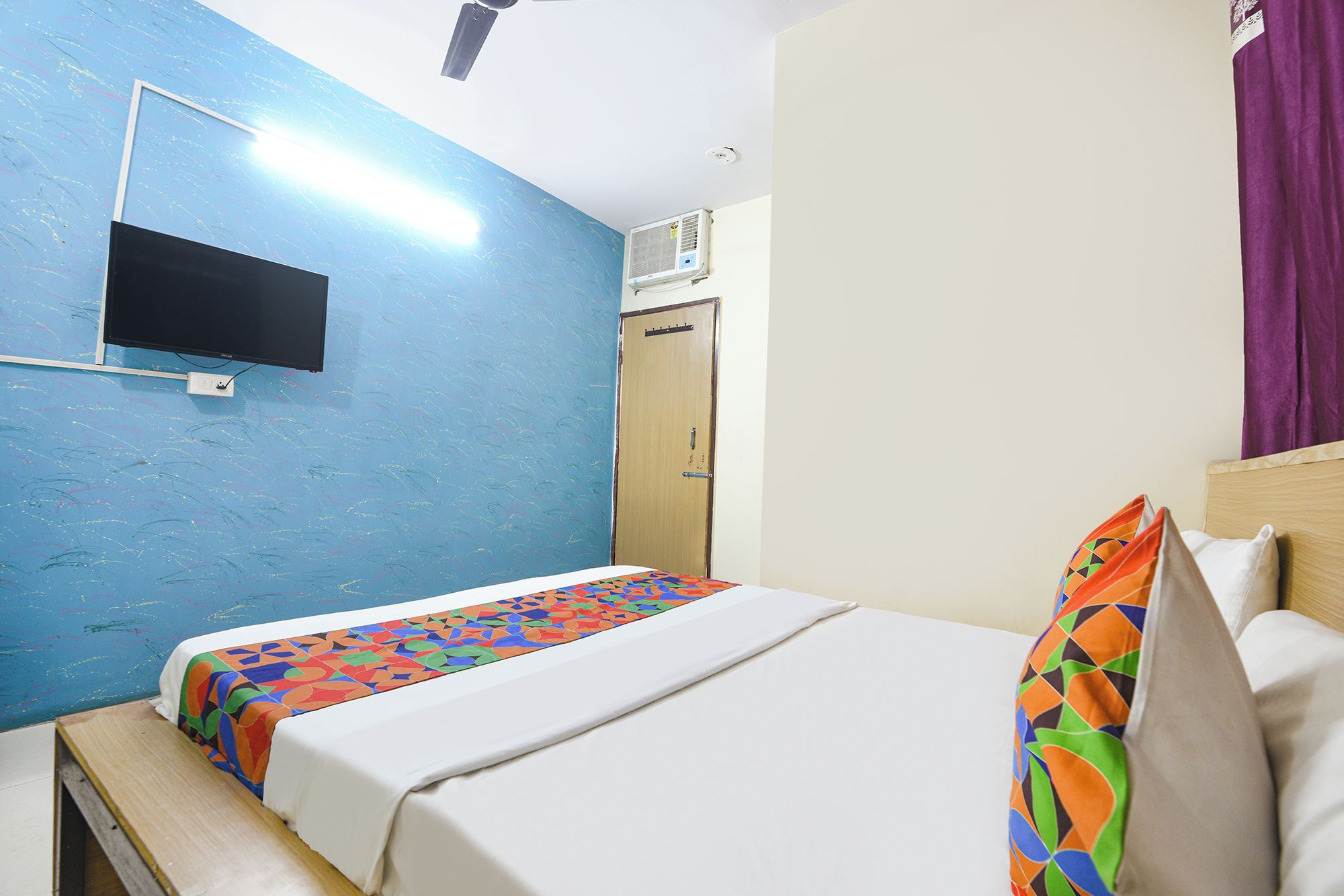 Quarto de hotel com cama, televisão na parede, ar condicionado e uma porta.