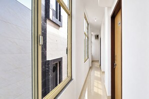 A corridor with a marble wall, a wooden door, and a window.