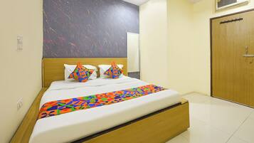 Habitación de hotel con una cama, cabecera de madera, colcha de diseño geométrico y pared lisa con textura, además de una puerta de madera.