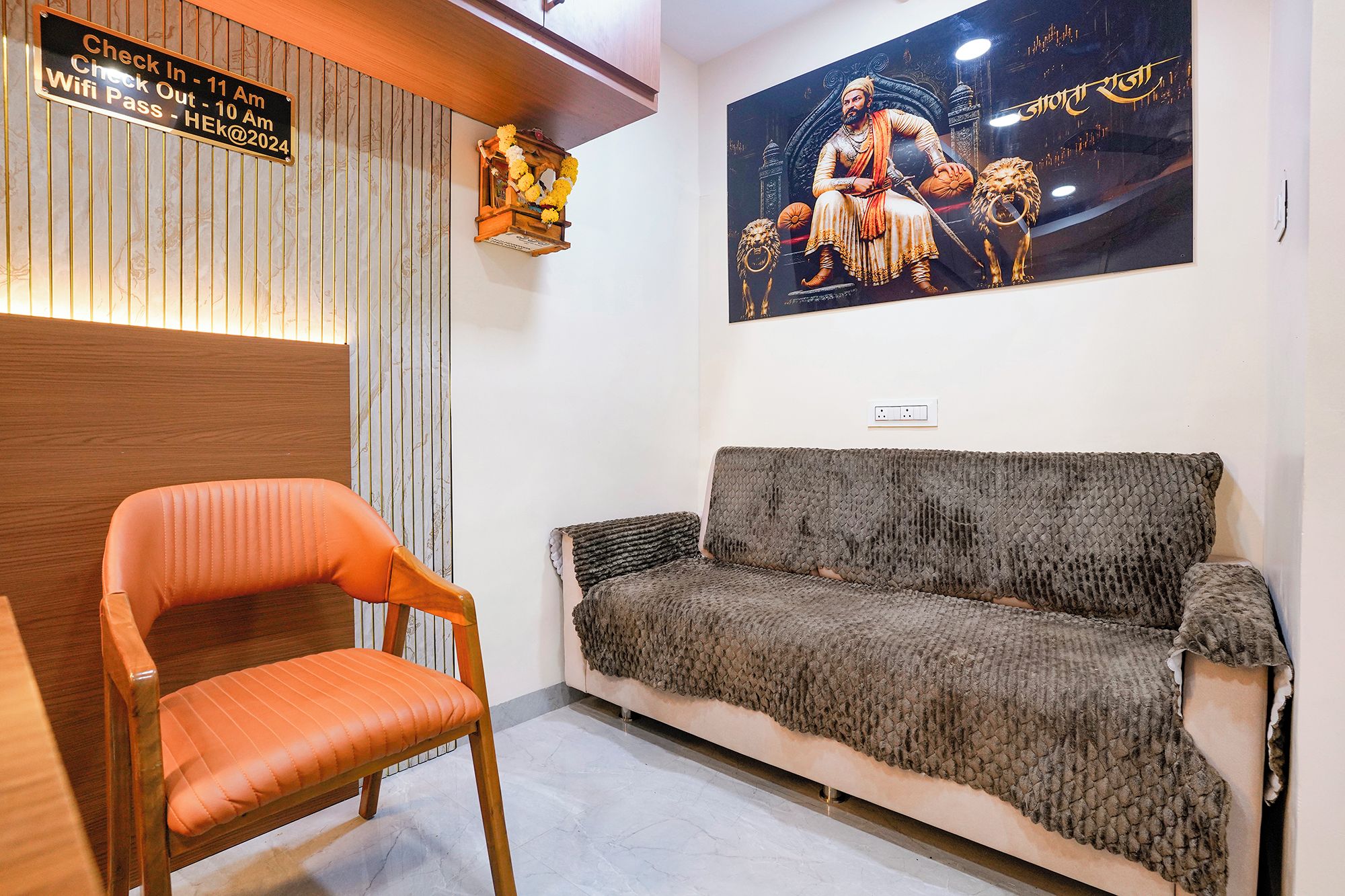A reception area with a wooden reception desk, a sofa, and a chair. There is a sign indicating check-in and check-out times and a WiFi pass.