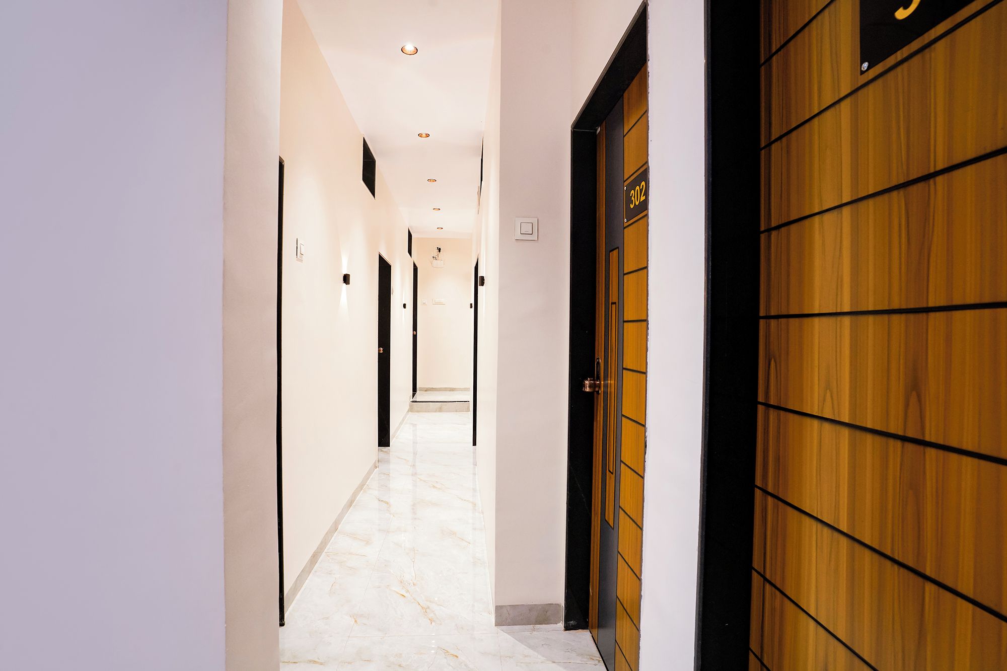 Un pasillo con una puerta de madera a la derecha, un cartel con el número 302 encima, y un piso de mármol.
