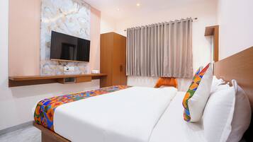 A hotel room with a bed, a TV mounted on the wall, a wooden wardrobe, and a window with curtains.