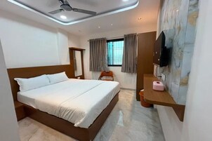 A hotel room with a bed, a ceiling fan, a TV, a window with curtains, and a small table with a pink object.