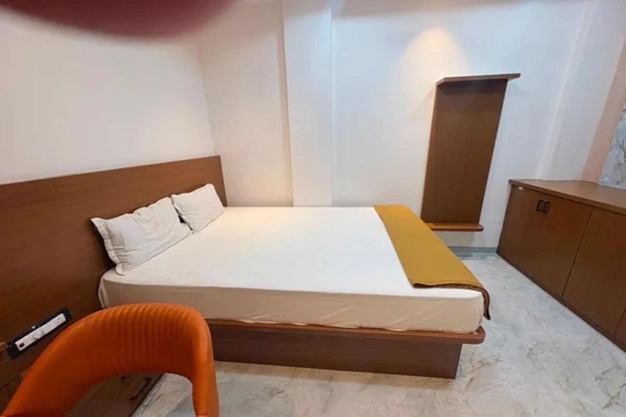 Hotellihuone, jossa on sänky, puinen pääty, yöpöytä, vaatekaappi ja tuoli.