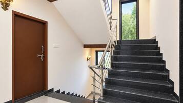 Un interior moderno con una puerta de madera, una escalera de escalones negros y un ventanal con vista a la vegetación.