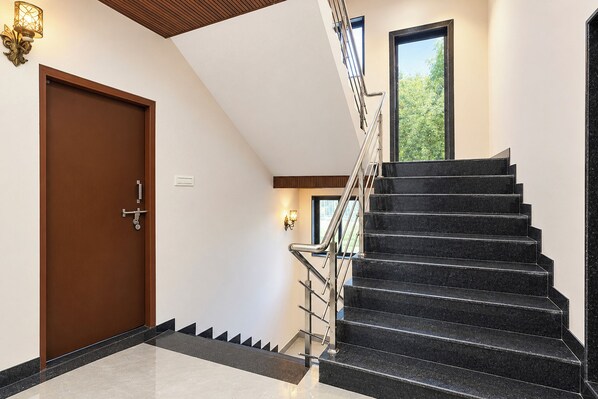 A modern interior with a wooden door, a staircase with black steps, and a window with a view of greenery. - FabHotel Ekta Inn (Chhatrapati Sambhajinagar)