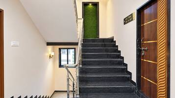 Una escalera con peldaños negros que conduce a una pared verde, una puerta de madera con una franja dorada y un cartel que indica los números de habitación 301 a 307.