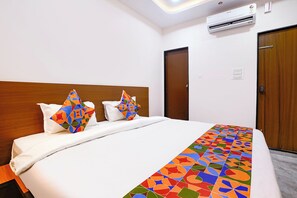 Una camera d'albergo con un letto, due cuscini, una testiera in legno, una porta e un condizionatore d'aria.
