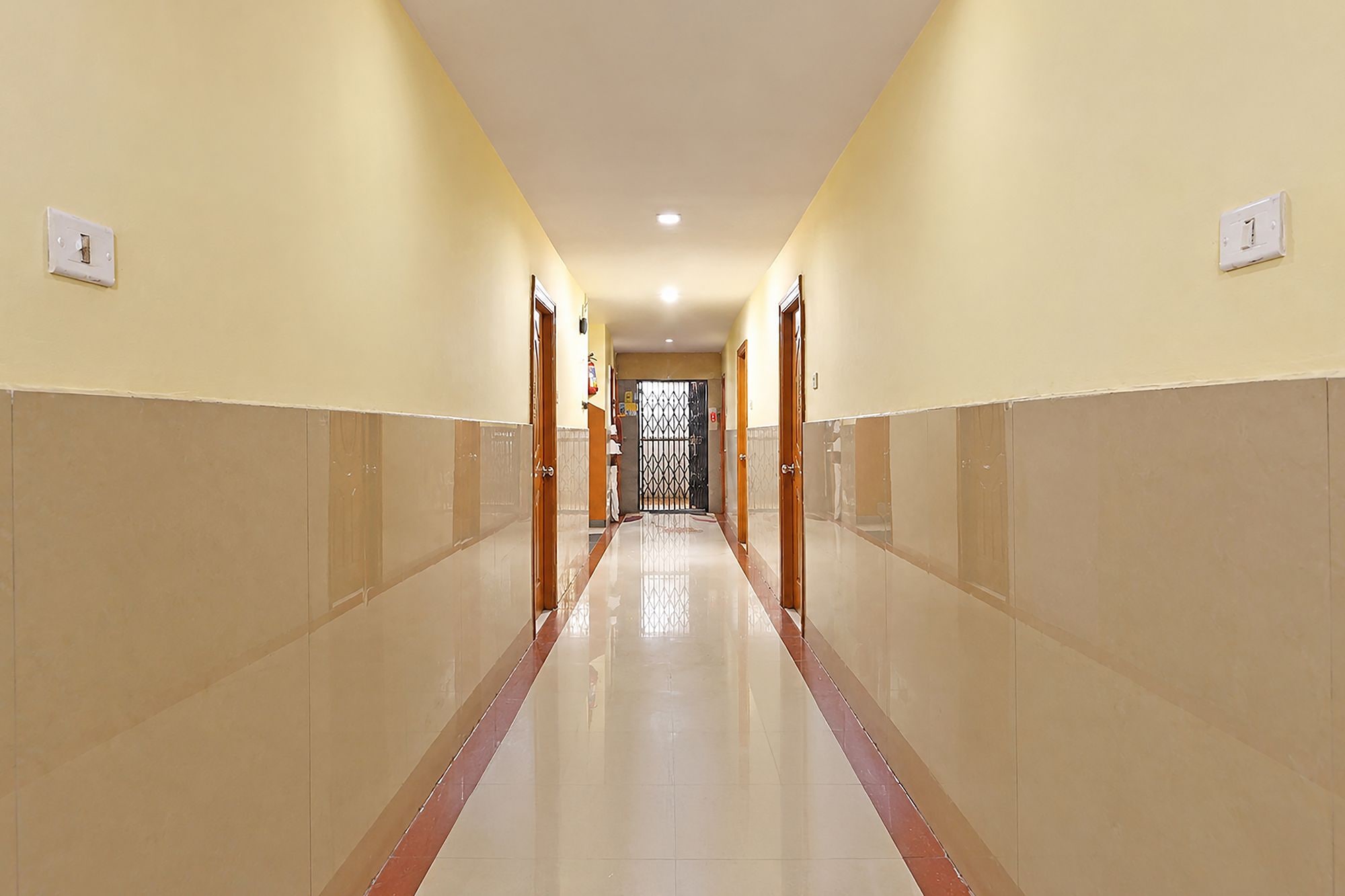 Pasillo de hotel con suelo de baldosas, puertas a ambos lados y una lámpara en el techo.