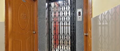 A wooden door with a number plate, a metal gate with a geometric pattern, and a wall-mounted light switch.