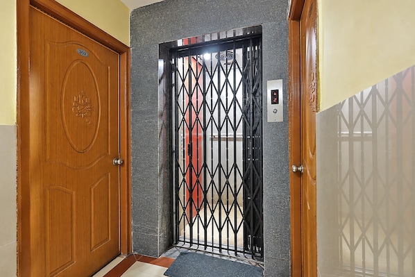 Una puerta de madera con una placa de número, un portón de metal con un diseño geométrico e interruptor de luz fijado a la pared.