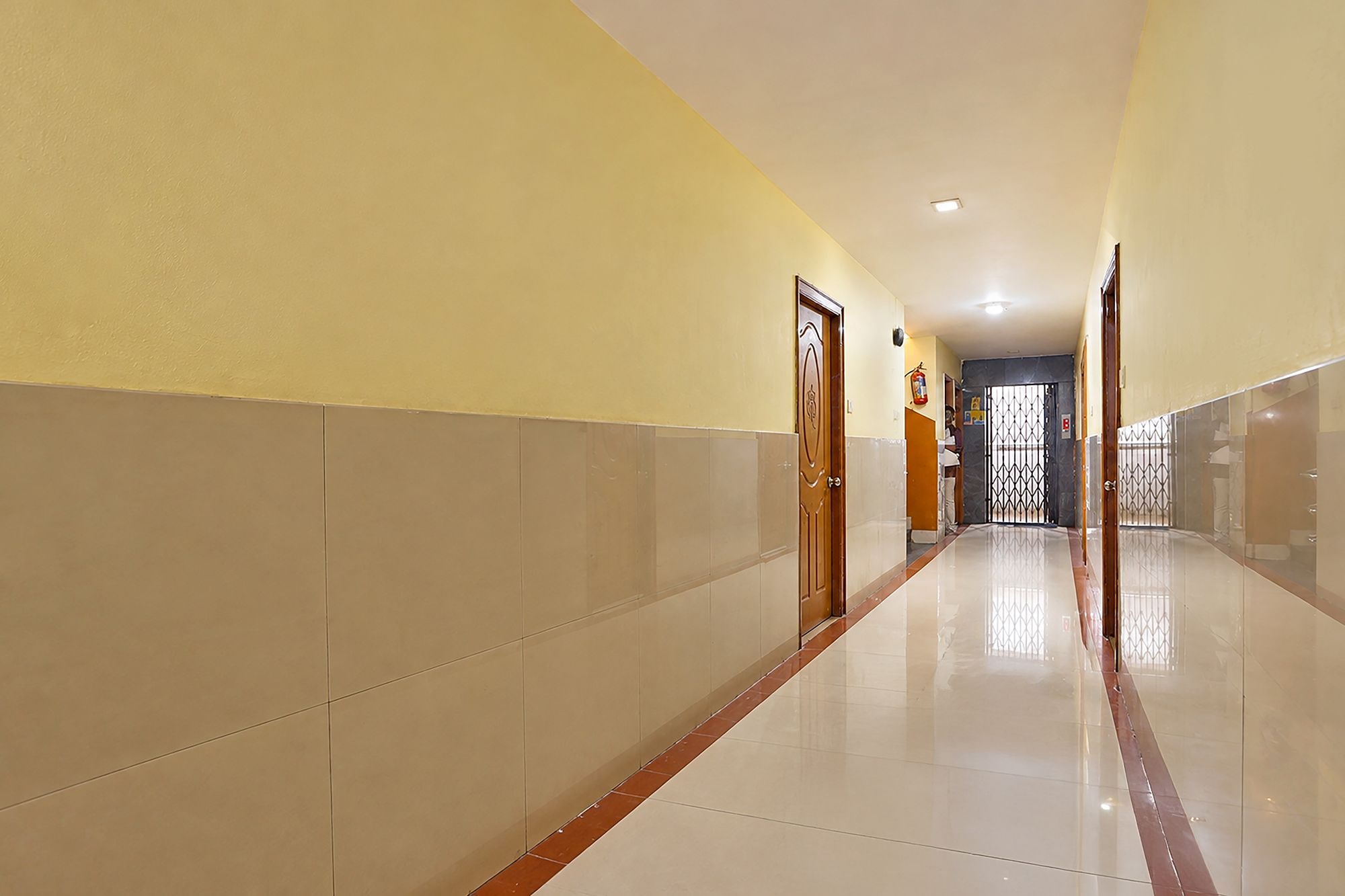 A corridor with a tiled floor, doors, and a fire extinguisher on the wall.
