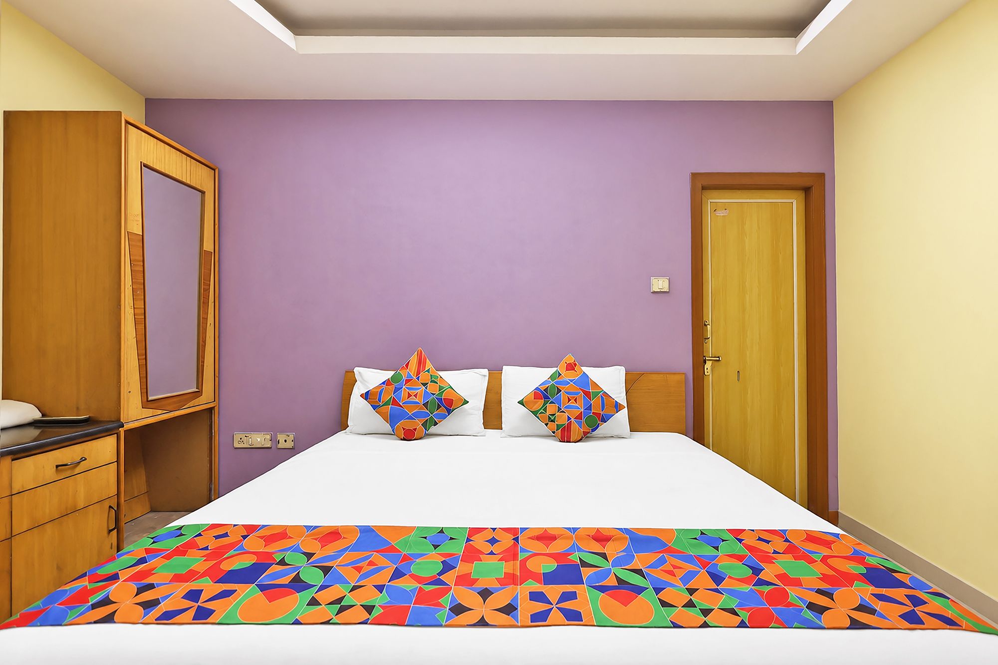 A bedroom with a bed, two pillows, a wooden wardrobe, and a door.