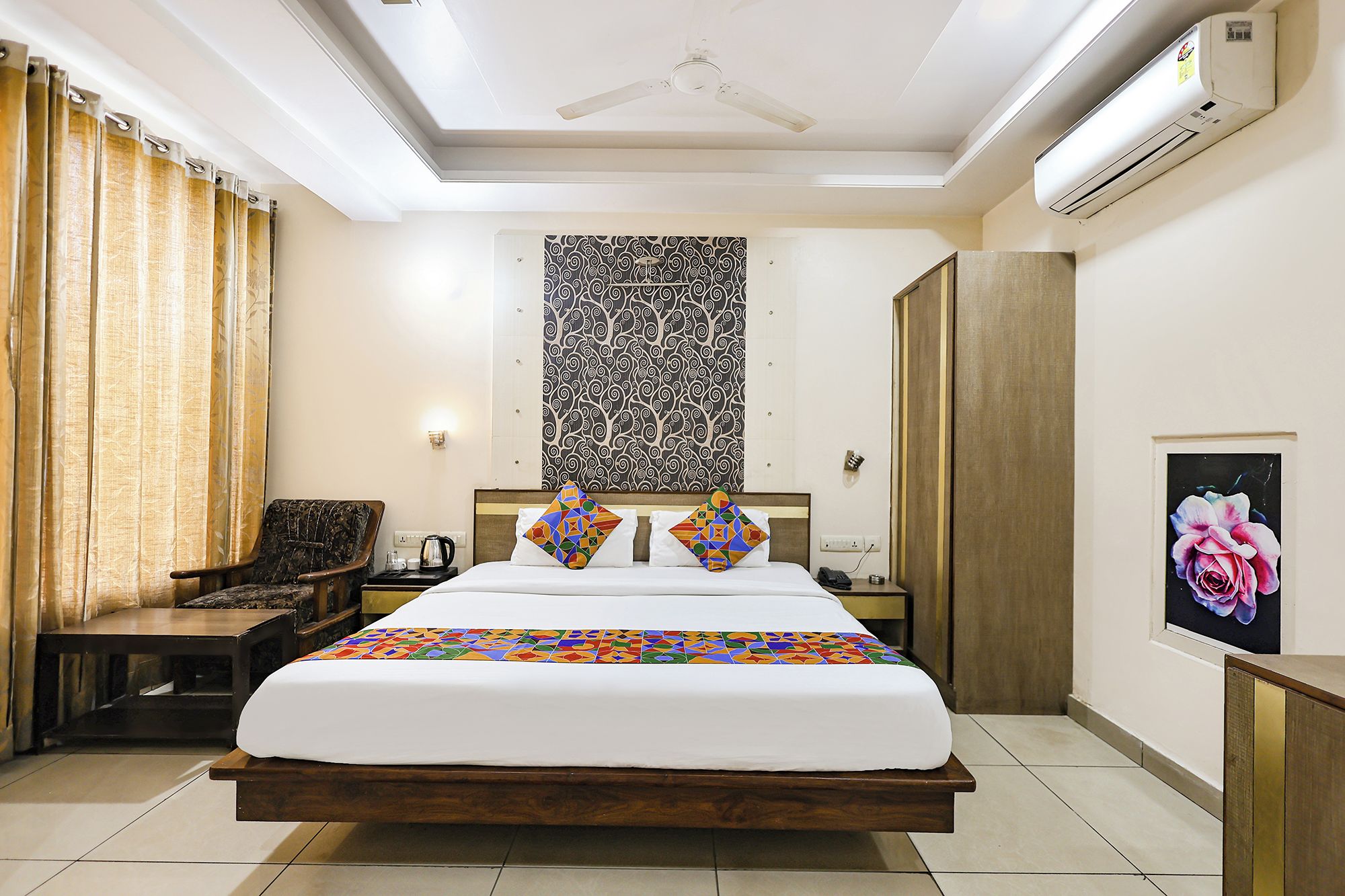 Habitación de hotel con cama, una silla, mesita de noche, equipo de aire acondicionado y un cuadro en la pared.