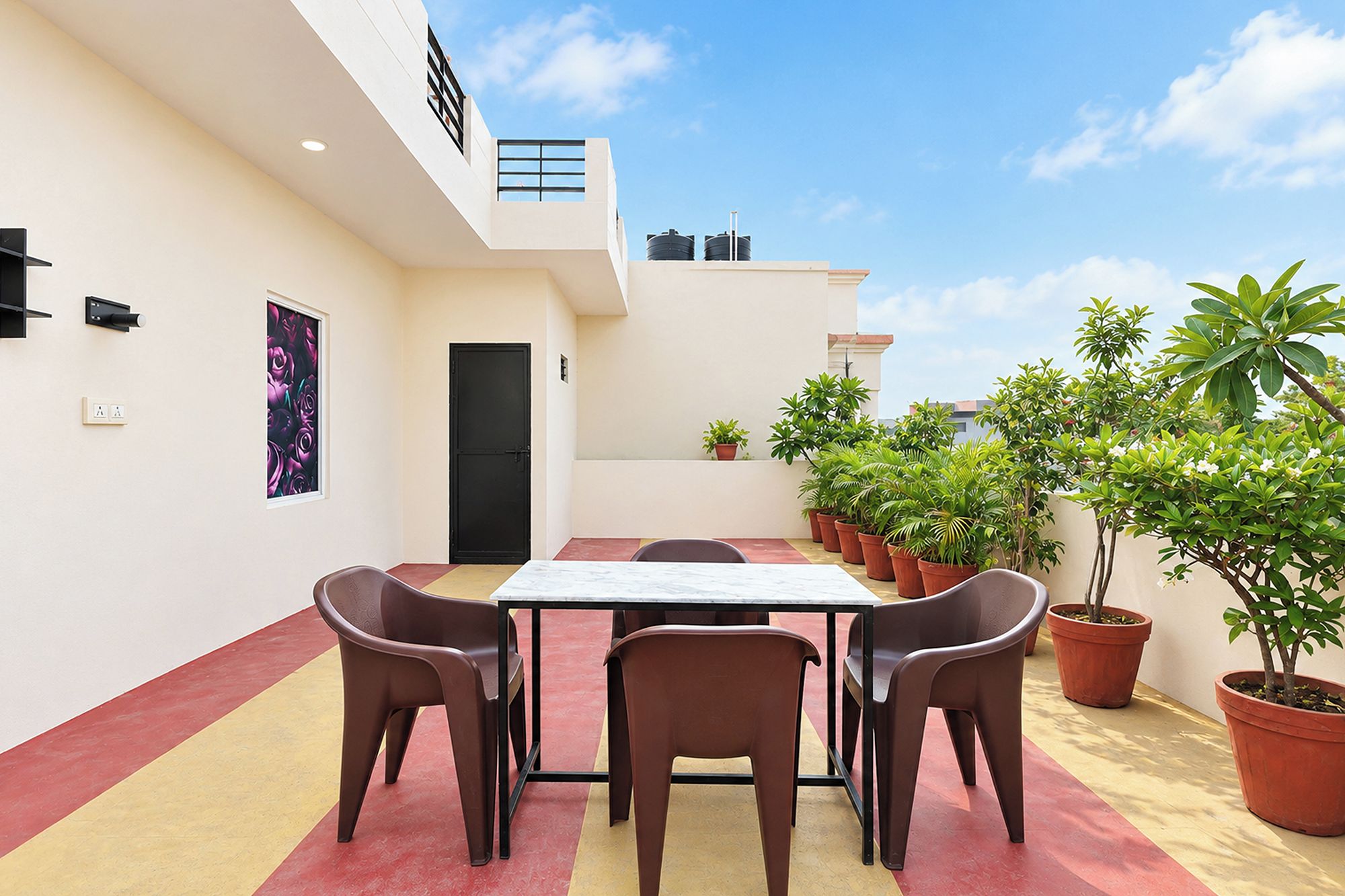A rooftop terrace with a table and chairs, potted plants, and a door.