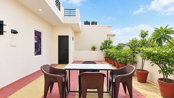 A rooftop terrace with a table and chairs, potted plants, and a door.