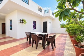 Un patio exterior moderno con una mesa y sillas de comedor, rodeado de plantas en macetas y un cielo despejado.