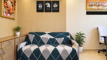 A room with a sofa, a desk, a chair, a potted plant, and framed artwork on the wall.