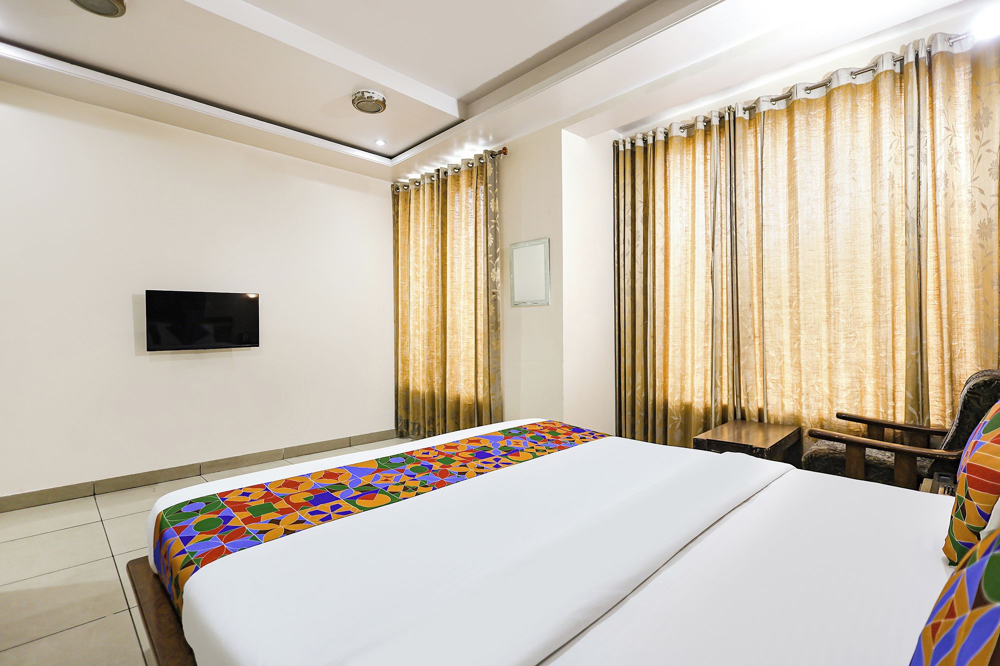 A hotel room with a bed, a television mounted on the wall, and curtains.