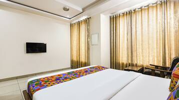 A hotel room with a bed, a television mounted on the wall, and curtains.