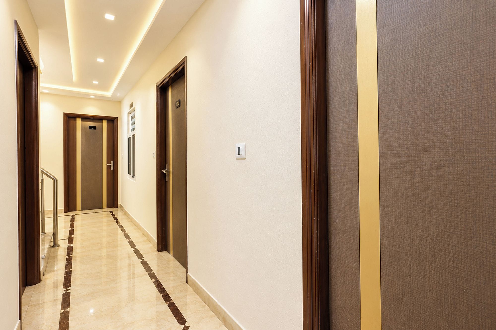 A hotel corridor with a marble floor, wooden doors, and a light switch on the wall.