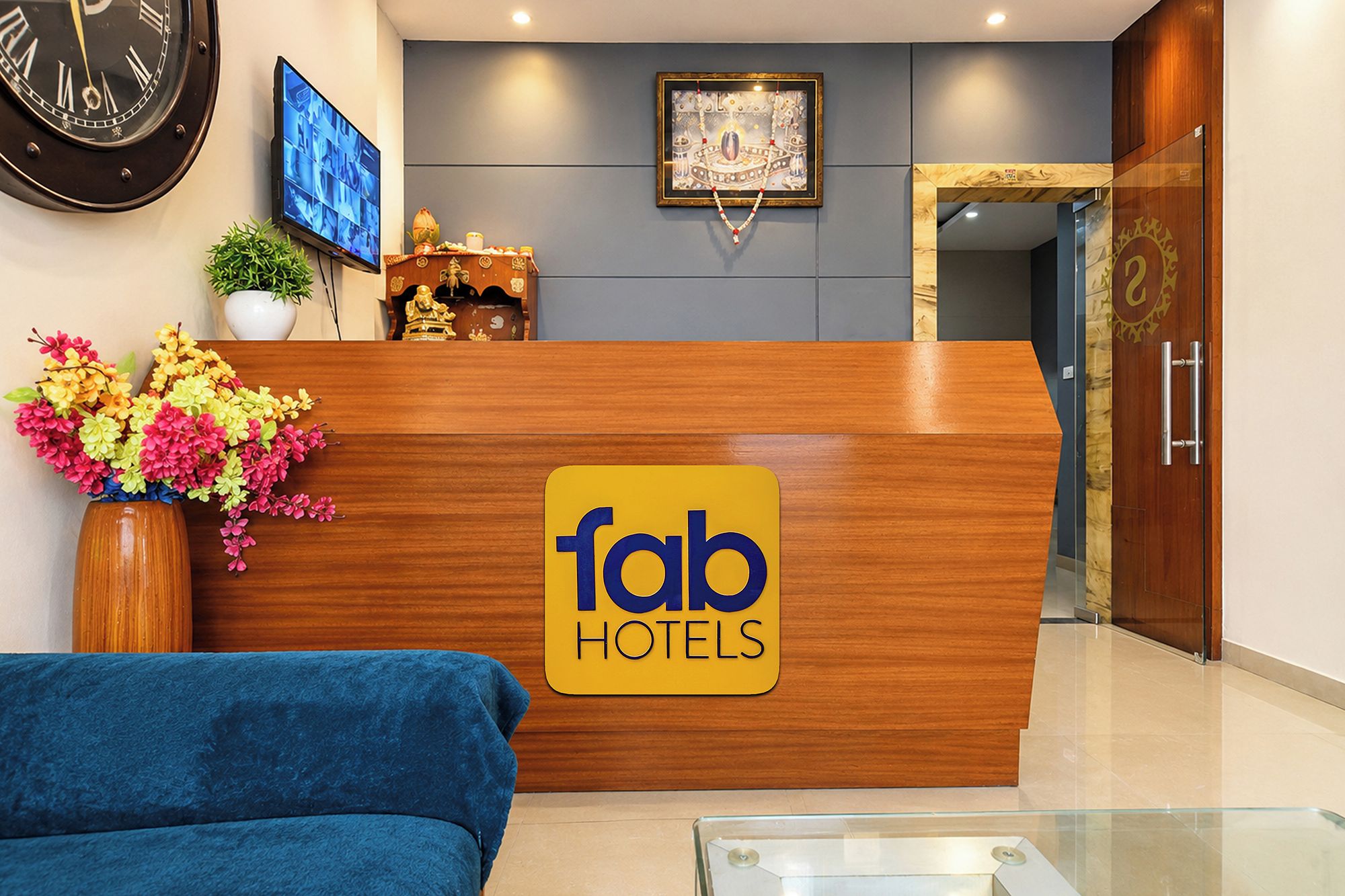 A reception desk with a 'fab hotels' sign, a clock, a television, and a decorative item on the wall.