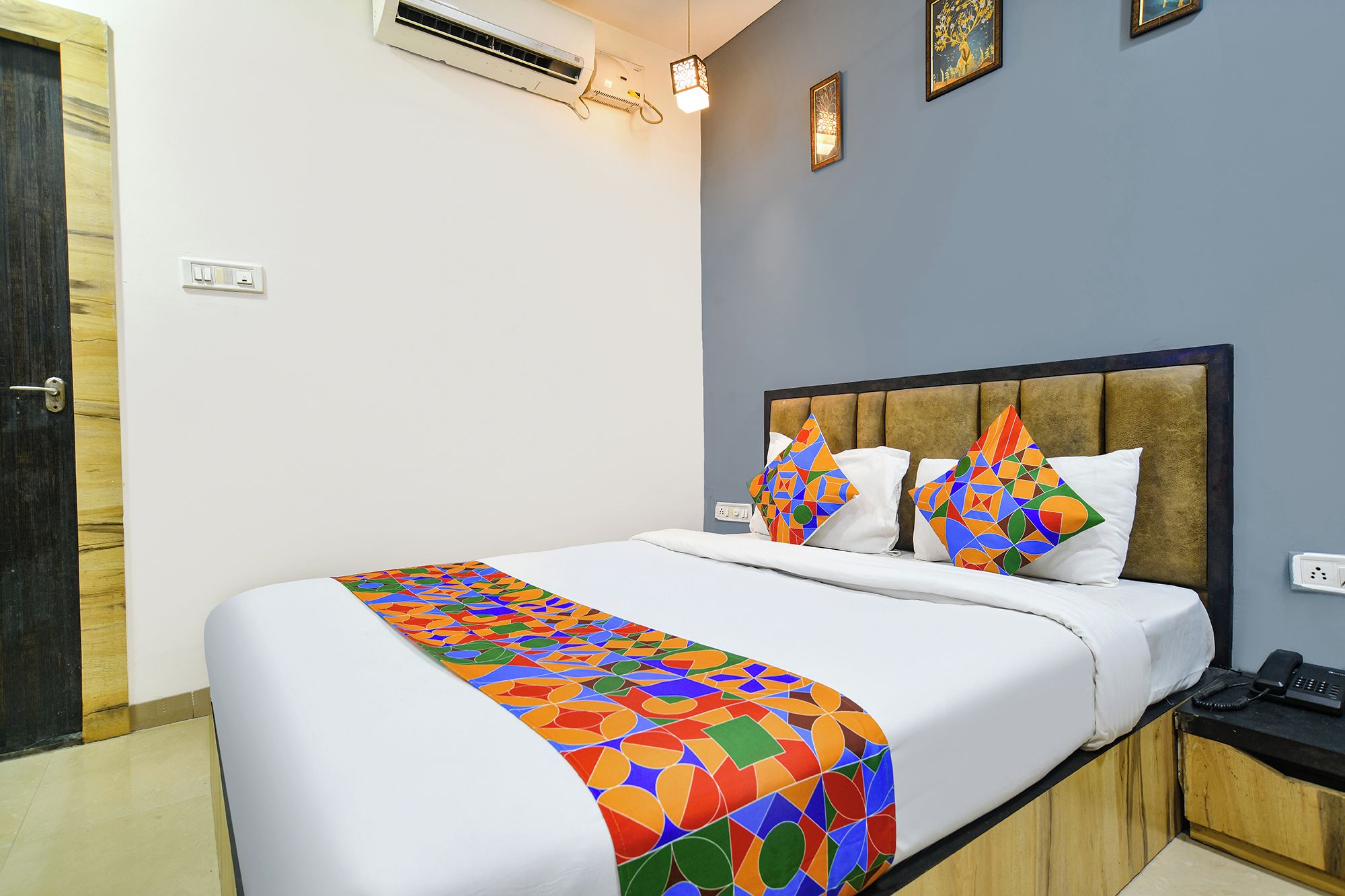 A hotel room with a bed, a bedside table, a phone, and a wall-mounted air conditioner.