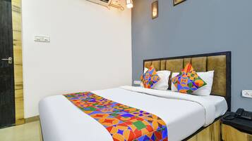 A hotel room with a bed, a bedside table, a phone, and a wall-mounted air conditioner.