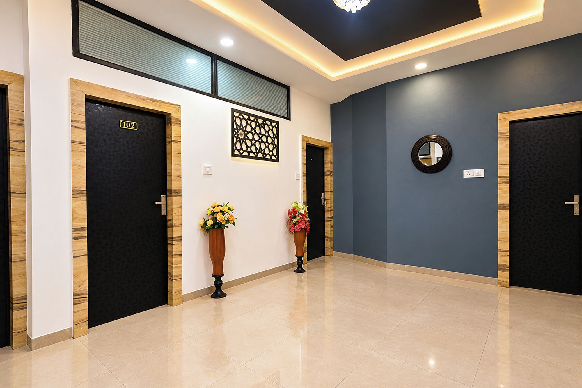 A hotel corridor with two black doors, one marked with the number 102, and a blue wall with a decorative panel and a round mirror.