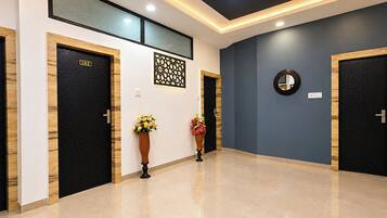 A hotel corridor with two black doors, one marked with the number 102, and a blue wall with a decorative panel and a round mirror.
