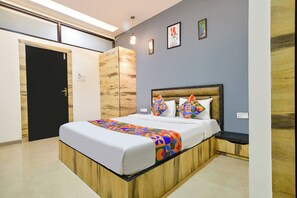 A modern bedroom with a wooden bed frame, a colorful bedspread, and a headboard with geometric pillows. - FabHotel Shivom (Indore)