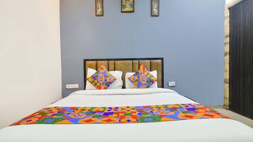 Ein Bett mit einer farbenfrohen, geometrisch gemusterten Tagesdecke, einem gepolsterten Kopfteil und zwei an der Wand befestigten Bilderrahmen darüber.