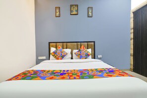 A bed with a colorful geometric-patterned bedspread, a headboard with a tufted design, and two wall-mounted picture frames above the bed. - Fabhotel Shivom (Indore)