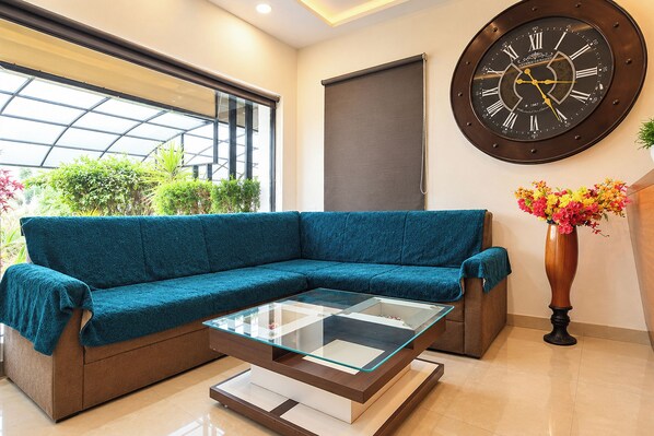 A modern living room with a teal sofa, a glass coffee table, and a large wall clock. - FabHotel Shivom (Indore)