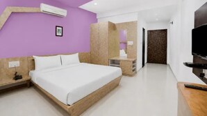 Un dormitorio moderno con una cama, mesitas de noche, un televisor y un baño a la vista al fondo.