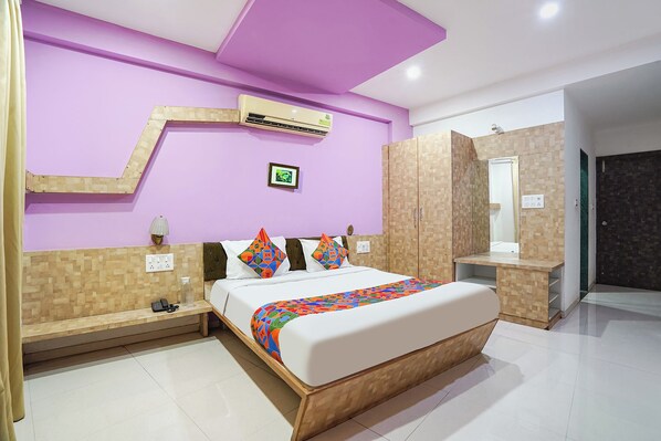 A modern hotel room with a large bed, a wooden headboard, a wall-mounted air conditioner, and a mirror above the bed.