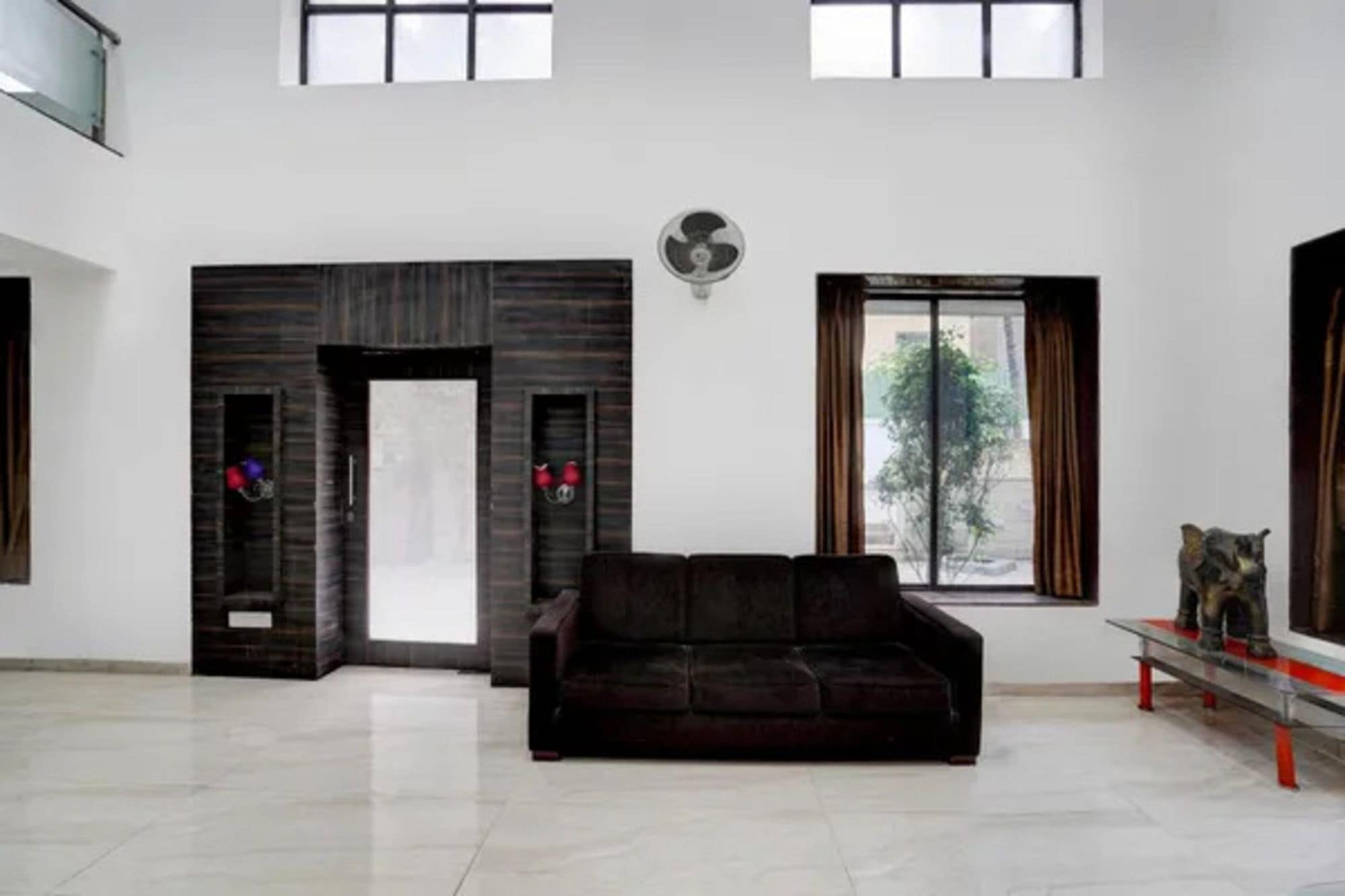 A spacious living room with a dark brown sofa, a white door, and a large window with a view of greenery.