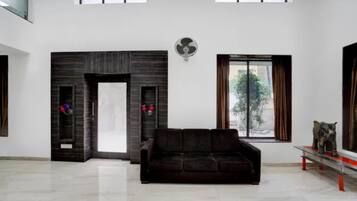 A spacious living room with a dark brown sofa, a white door, and a large window with a view of greenery.