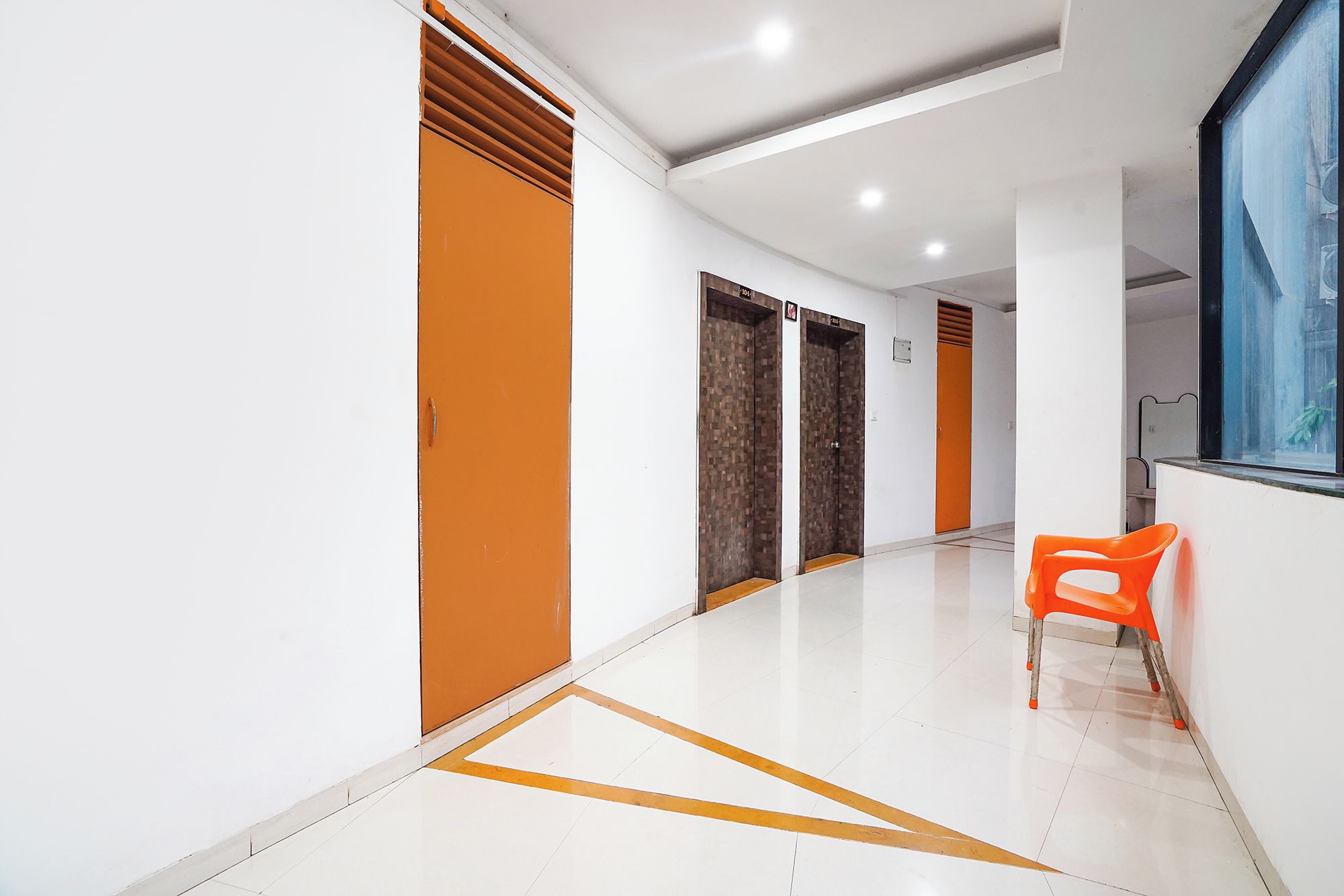 Un pasillo con dos puertas, una con panel marrón y la otra con textura de madera, que conduce a una habitación con ventana.