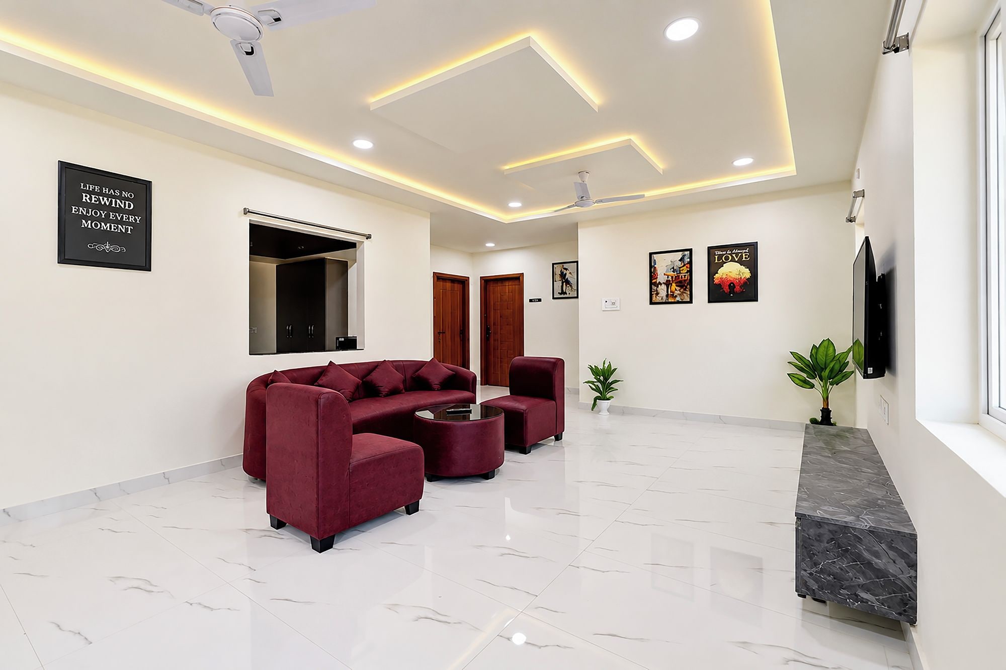 A modern lobby with a marble floor, a red sofa set, a flat-screen TV, and a ceiling with recessed lighting.