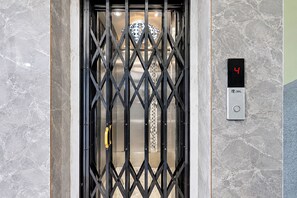 Un ascenseur doté d’une porte en treillis métallique, d’un écran numérique affichant le chiffre 4 et du logo Trego sur le mur.
