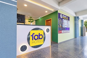 A hotel reception area with a 'fab hotels' sign, a reception desk, a green wall, and a 'WAAH HOME STAY FACILITIES' sign listing amenities.