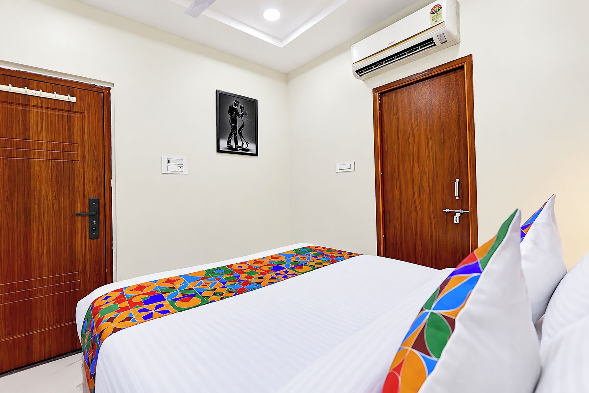 Une chambre d’hôtel avec un lit, deux portes en bois, un appareil de climatisation et un seul luminaire fixé au mur.