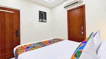 Une chambre d’hôtel avec un lit, deux portes en bois, un appareil de climatisation et un seul luminaire fixé au mur.