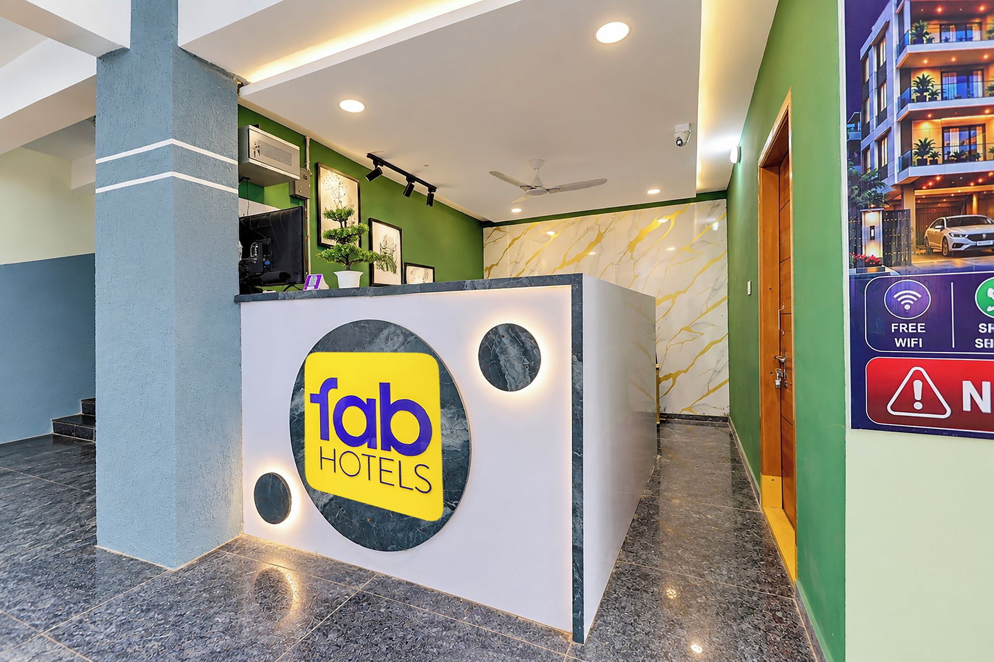 Een receptiebalie met een Fab Hotels logo, een plafondventilator en een bordje dat gratis WiFi en een shuttle service aangeeft.