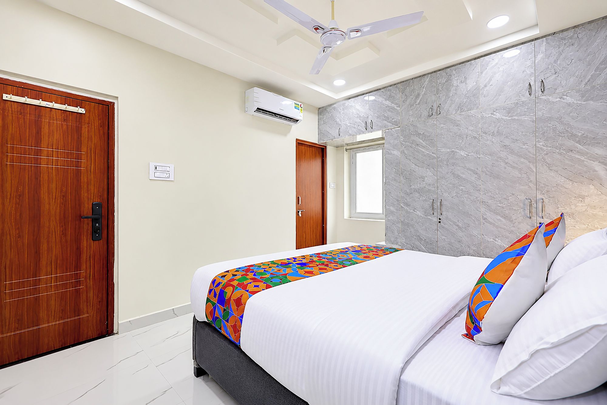 Quarto de hotel com cama, ventoinha no teto, parede de mármore e porta de madeira.